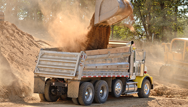 image of dump truck being filled with sand by an excavator